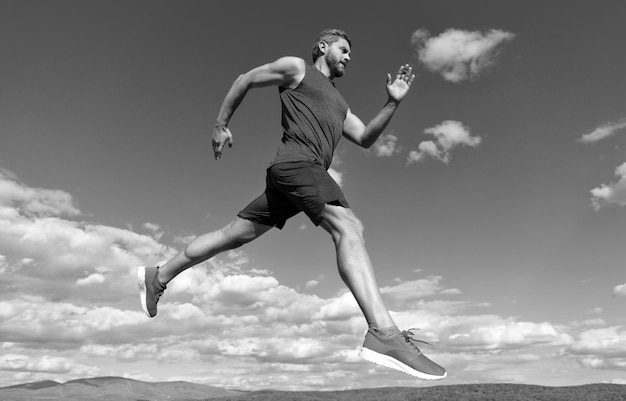 Healthy sportsman sprinter with muscular body running in sportswear outdoor on sky background stamina