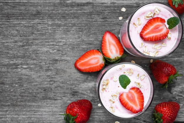 Healthy strawberry yogurt with oats and mint in glasses with fresh berries over rustic wooden table