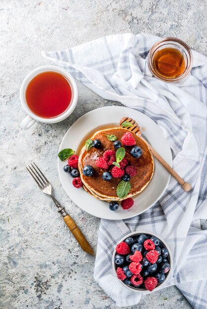 Healthy summer breakfast,homemade classic american pancakes with fresh berry and honey, morning light grey stone surface  top view