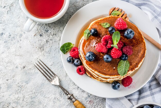 Healthy summer breakfast,homemade classic american pancakes with fresh berry and honey, morning light grey stone surface  top view