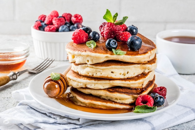 Foto sana colazione estiva, pancake americani classici fatti in casa con bacche fresche e miele, superficie di pietra grigio chiaro mattutina