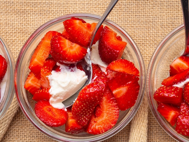 Healthy summer breakfast strawberry slices with cream in glass bowls on rustic sackcloth background