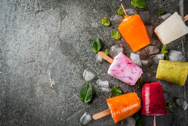 Dolci dessert estivi. ghiaccioli al gelato. succhi tropicali congelati, mirtilli di frullati. ribes, arancia, mango, kiwi, banana, cocco, lampone. sul tavolo di pietra nera, vista dall'alto