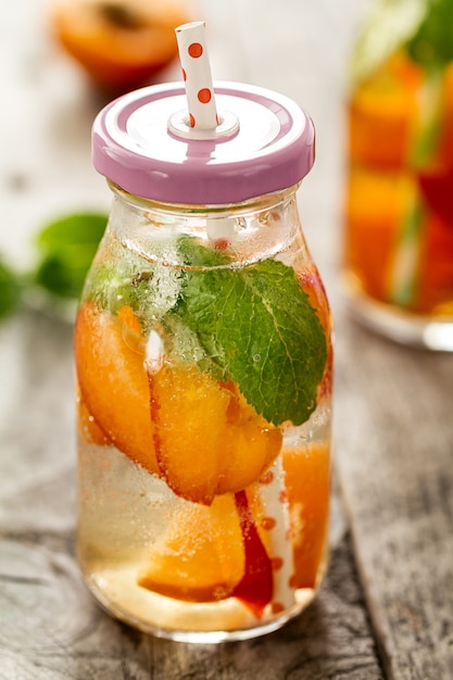 Healthy tasty fresh refreshing detox water in bottles or jars with apricots, mint and ice on wooden background. Closeup. Healthy Life Concept.