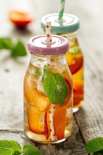 Здоровая вкусная свежая освежающая вода детоксикации в бутылках или баночках с абрикосами, мятой и льдом на деревянном фоне. Крупный план. Концепция здоровой жизни.