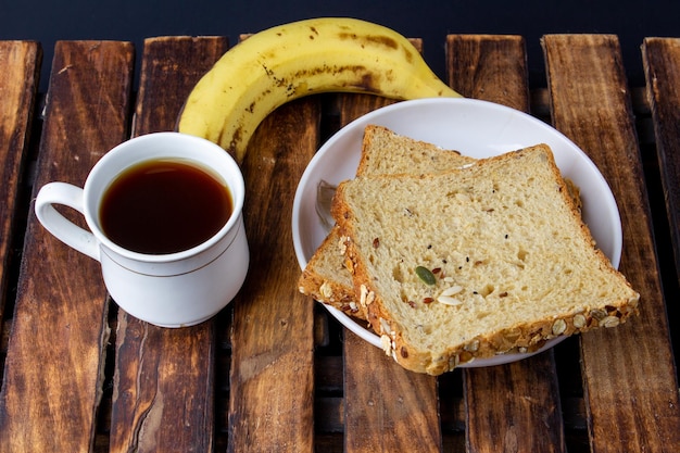 Sana gustosa colazione mattutina con pane multicereali caffè nero e banana su legno