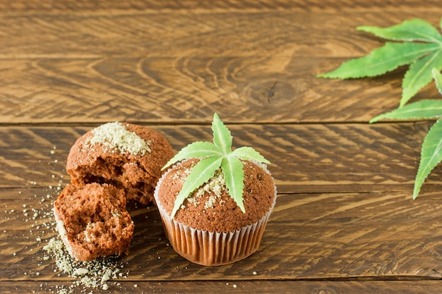Healthy and tasty vegan and gluten free muffins topped with hemp seeds on a white plate on wooden table. marijuana cupcake muffins with cannabis leaves