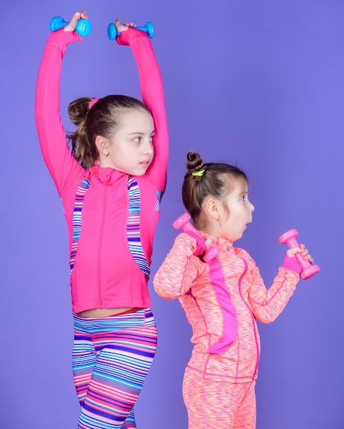 Healthy upbringing Sporty babies Following her sister Girls cute kid exercising with dumbbells Motivation and sport example concept Toddler repeat exercise after sister Sport exercises for kids