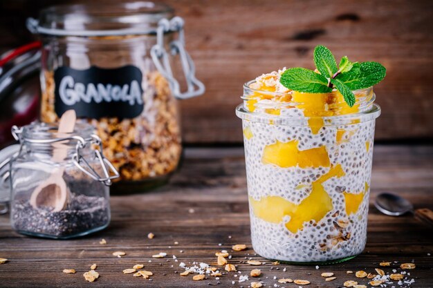 Healthy vegan breakfast chia pudding with mango and granola in the jar on wooden rustic background