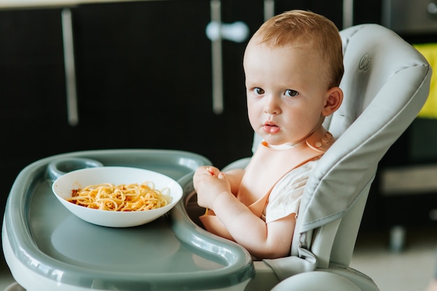 Healthy vegan breakfast tasty pasta with red sauce is eaten by a very nice and cute baby boy carefre...