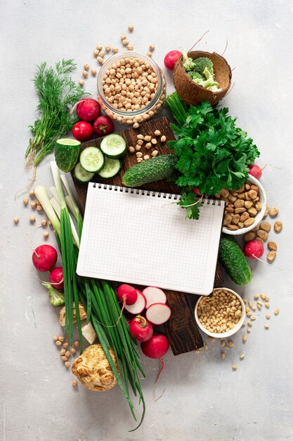 Healthy vegan food concept. Blank notebook with fresh vegetables, herbs, legumes and nuts. Veggie Cooking Concept