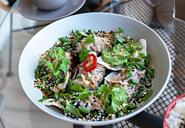 Healthy vegan food jiaozi with tofu and vegetables in soy sauce with parsley and cilantro in plate on glass table chinese dish