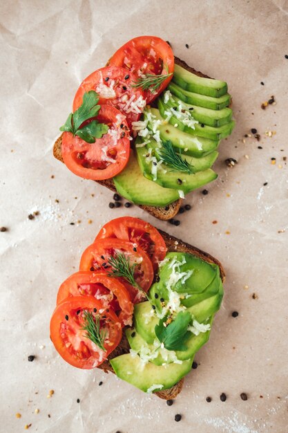 Vegano sano panino fatto in casa, avocado e pomodori con pane di grano scuro su uno sfondo di carta.