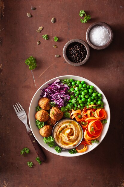 Healthy vegan lunch bowl with falafel hummus carrot ribbons cabbage and peas