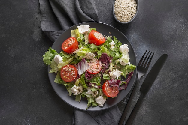 Healthy vegan salad in black dish with fresh tomato, greens, seeds hemp for clean eating. Top view.