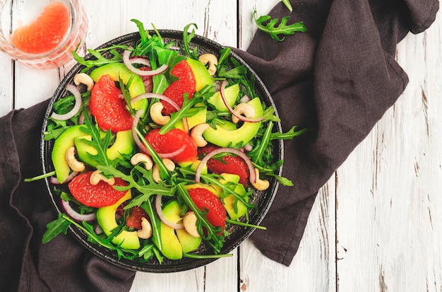 Healthy vegan vegetarian lunch salad with arugula avocado grapefruit and cashews and dressing of olive oil honey and wine vinegar White rustic kitchen table top view