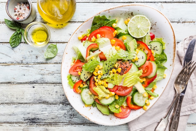 Здоровый овощной салат из свежих помидоров, огурцов, салата и кукурузы на тарелке, вид сверху меню диеты