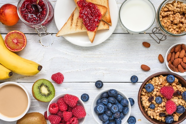 Photo healthy vegetarian breakfast buffet with various morning food frame made of granola coffee toast fruit berries nuts orange juice on white wooden table top view with copy space