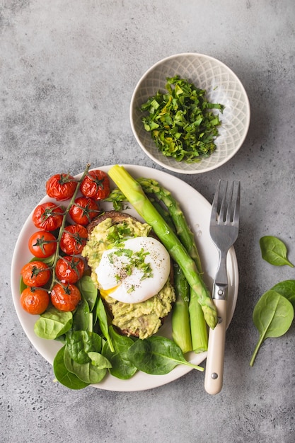 Healthy vegetarian meal plate. Toast, avocado, poached egg, asparagus, baked tomatoes, spinach.