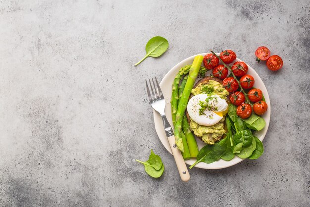 Healthy vegetarian meal plate. Toast, avocado, poached egg, asparagus, baked tomatoes, spinach.