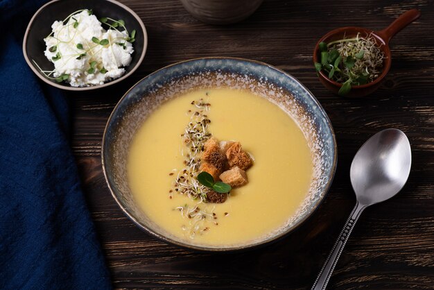 Zuppa di purea vegetariana sana, piatto di zuppa di crema di zucca con crostini di pane, formaggio e microgreens su uno sfondo di legno scuro.