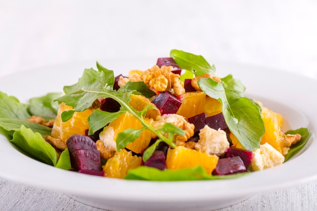 Healthy vegetarian salad with beetroot green arugula orange feta cheese and walnuts on white plate close up