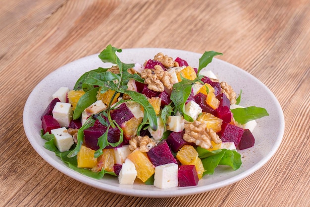 Healthy vegetarian salad with beetroot green arugula orange feta cheese and walnuts on white plate close up