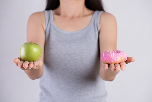 Sano contro malsano. ciambella della tenuta della mano della donna e mela verde.