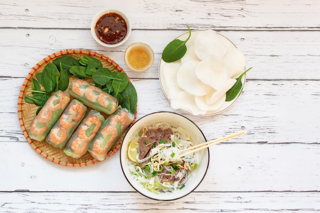 Sano cibo vietnamita primo piano di involtini primavera pho bo zuppa vietnamita con noodles e patatine di riso di manzo su una tavola di legno salsa di sesamo