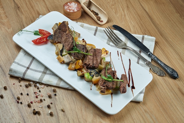 Healthy warm salad with grilled beef and vegetables on a white ceramic plate. Composition with salad and spices on a wooden table. Food photography