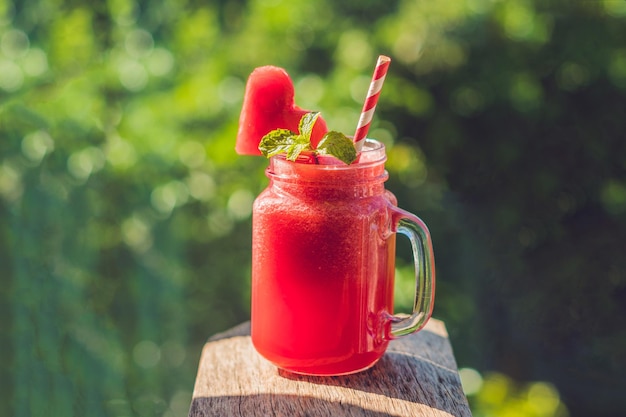 Healthy watermelon smoothie in Mason jars with mint and striped straws against the background of greenery.