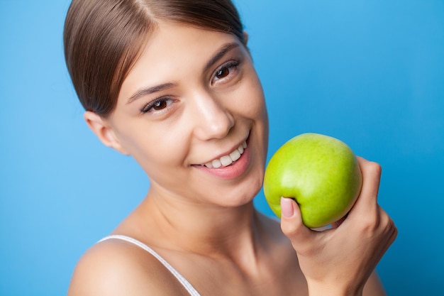 Ritratto di denti bianchi sani di donna sorridente sportiva con mela verde