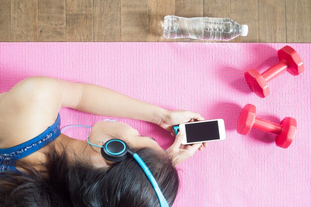 Healthy woman listening music by smart phone with dumbbells 