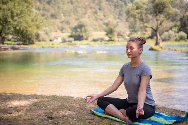 healthy woman relaxing while meditating and doing yoga exercise in the beautiful nature on the bank of the river