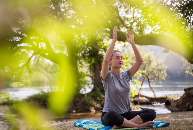 Photo healthy woman relaxing while meditating and doing yoga exercise in the beautiful nature on the bank of the river