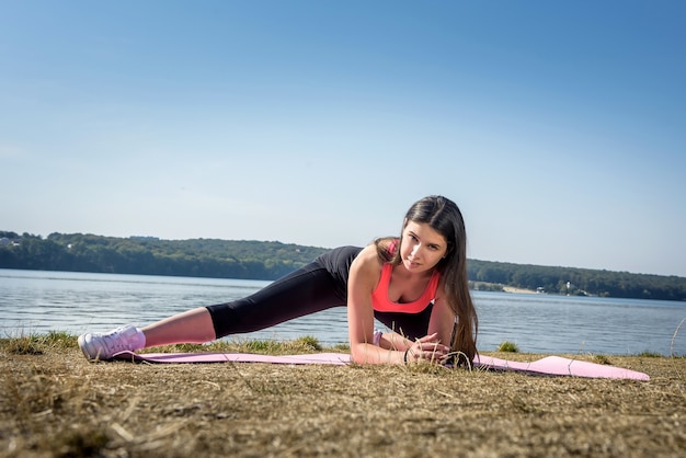 Healthy woman resting and doing  stretching excercise outdoor near the lake.