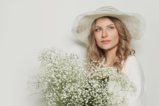 Healthy woman wearing summer season hat holding flowers on white background