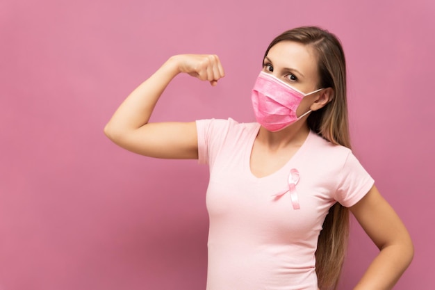 Healthy woman with her arm up as sign of strengh of fight against cancer ribbon icon on her chest