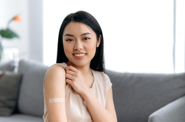 Photo healthy young asian woman protected from viruses in tshirt and with a plaster on her shoulder received vaccine against covid 19 or influenza immunity from infections takes care of her health
