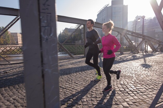 Foto giovane coppia in buona salute che fa jogging in città al mattino presto con l'alba sullo sfondo