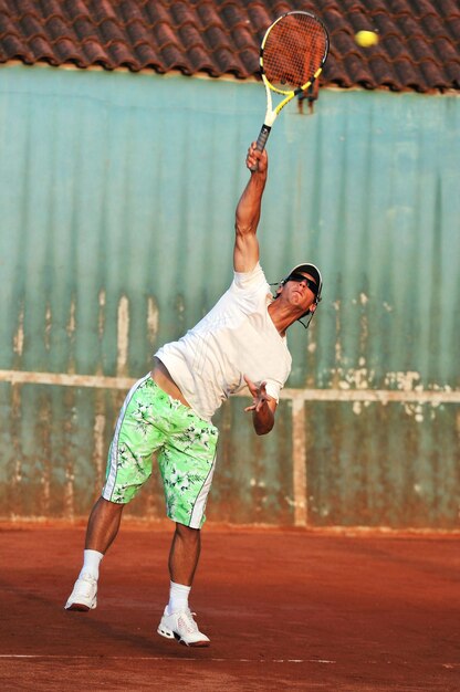 Фото Здоровый молодой человек играет в теннис с другом на открытом воздухе