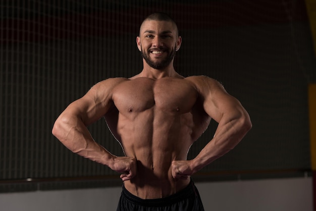 Photo healthy young man standing strong in the gym and flexing muscles  muscular athletic bodybuilder fitness model posing after exercises