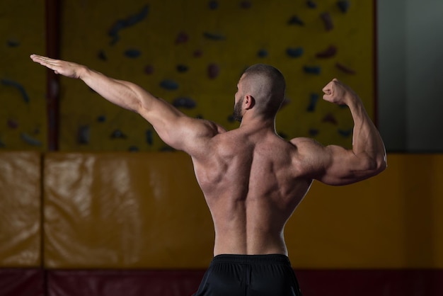 Healthy Young Man Standing Strong In The Gym And Flexing Muscles  Muscular Athletic Bodybuilder Fitness Model Posing After Exercises