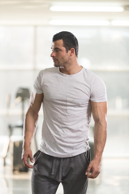 Healthy Young Man in White Tshirt Standing Strong and Flexing Muscles  Muscular Athletic Bodybuilder Fitness Model Posing After Exercises