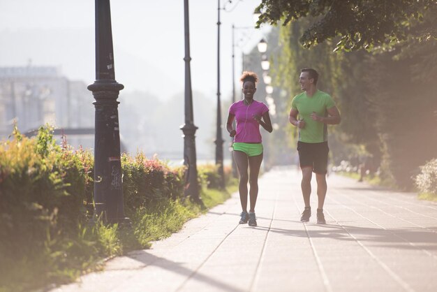 日の出を背景に早朝に市内でジョギングをしている健康な多民族の若いカップル