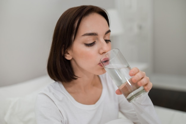 Healthy young woman drinking fresh water after waking up closeup