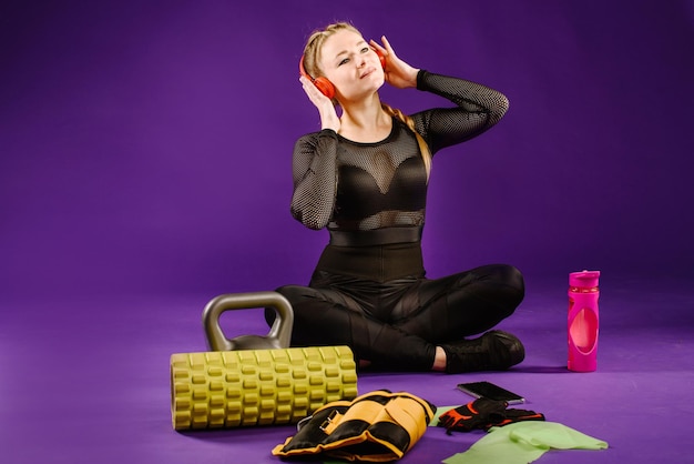 Healthy young woman relaxing after training session on the purple background. listening music in headphones
