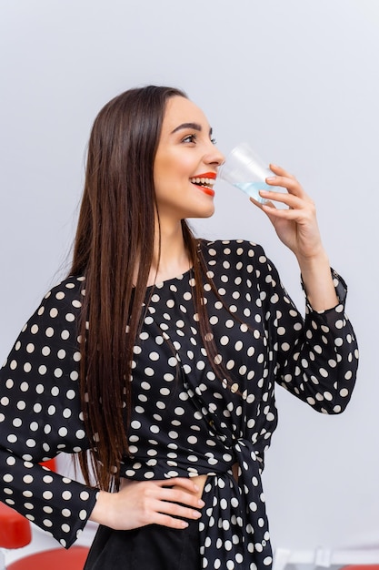 Healthy young woman with glass of fresh water on white background Brunette girl with red lips and long hair