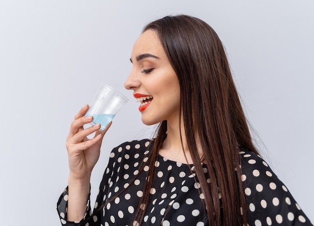 Healthy young woman with glass of fresh water on white background. Brunette girl with red lips and long hair.