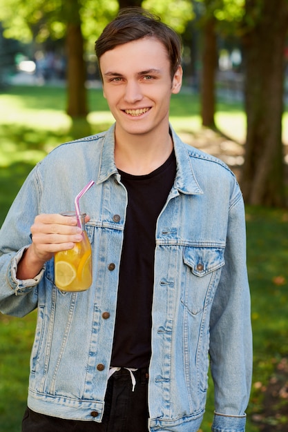 Healthy youth lifestyle. Happy hipster guy with detox with sweet citrus detox tea or orange juice in summer, on green nature background.